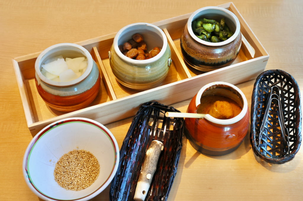 お漬物（紀州小梅・ゆず大根・青きゅうり）と新鮮生ドレッシング、ごまが入ったすり鉢がテーブルに到着